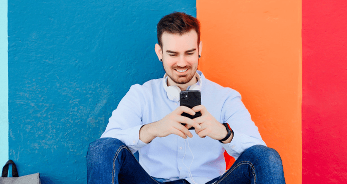 Man sitting, smiling at smartphone, colorful background.