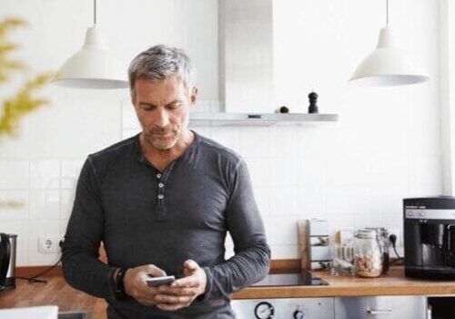 A man standing in the kitchen looking at his phone.