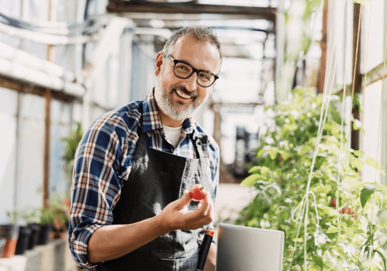 A man holding tomatoes in his hand and smiling.