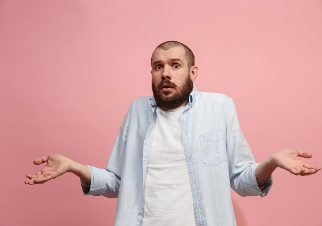 A man standing in front of a pink wall with his arms outstretched.